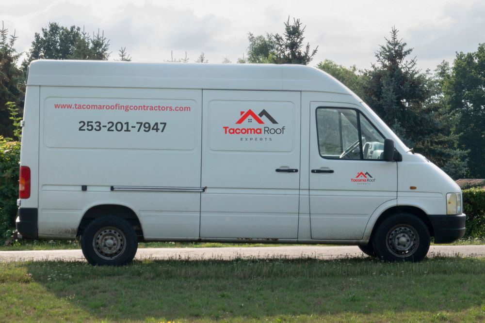 A white van on grassy terrain, featuring a sign advertising roofing services in Tacoma, WA.