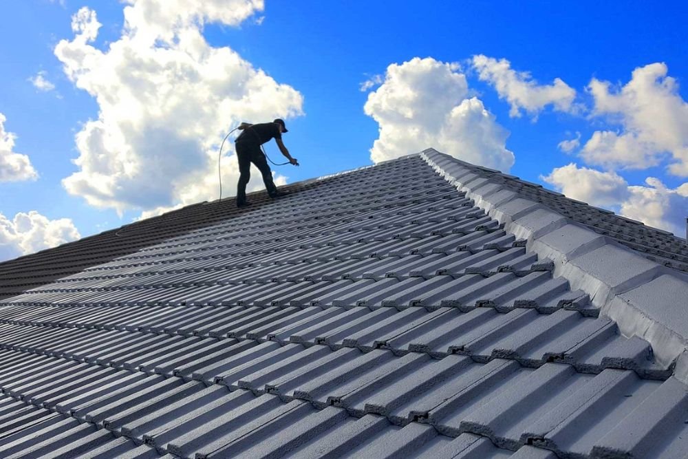 A man is positioned on a rooftop against a bright blue sky, symbolizing roofing services in Tacoma, WA.