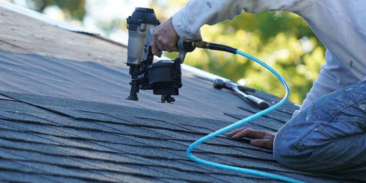 A man employs a nail gun to install a roof, illustrating the necessity of recognizing signs that indicate roof repair services are needed.