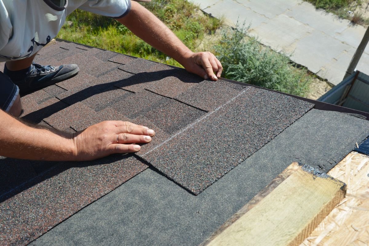A man installs a roof shingle on a house, contributing to the ongoing roof replacement process. 
