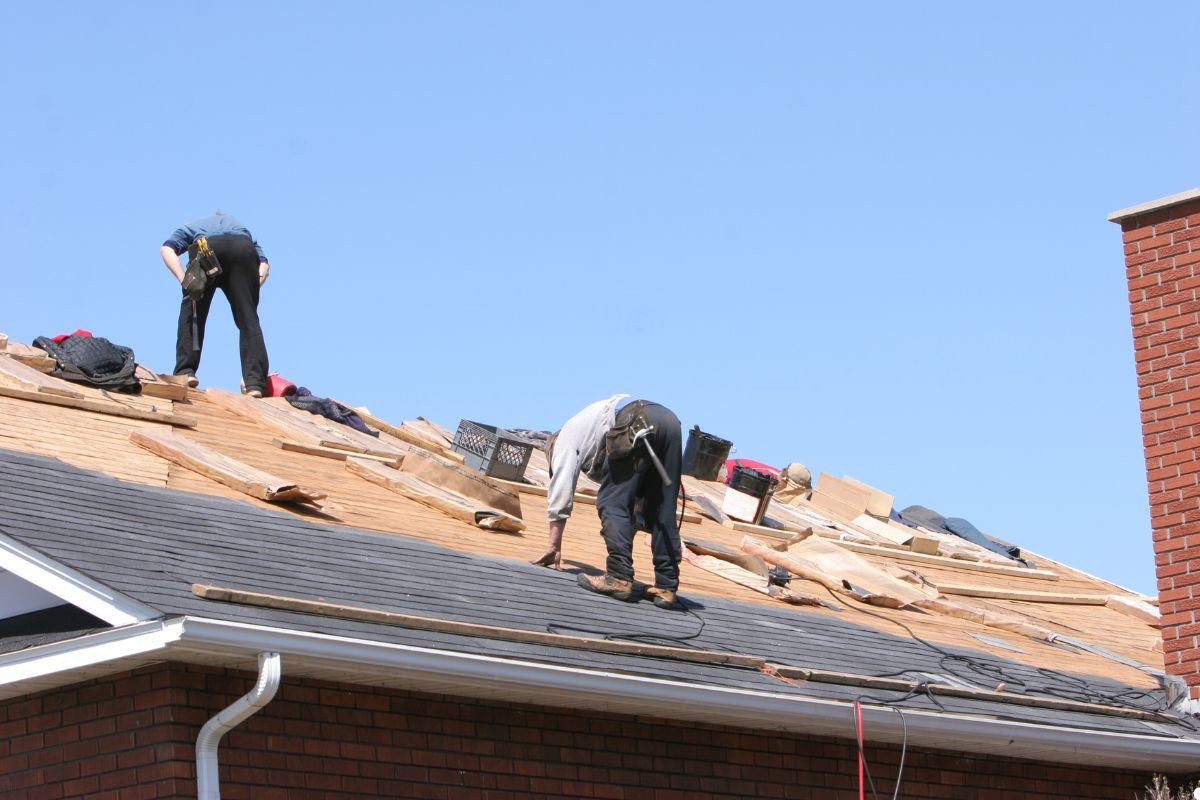 Three men installing roofing materials under a clear blue sky, focused on their work and collaborating effectively.